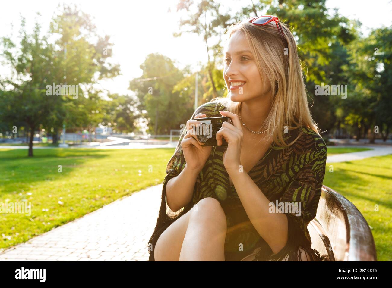 Beautiful happy young blonde woman sitting on a bench at the city park ...