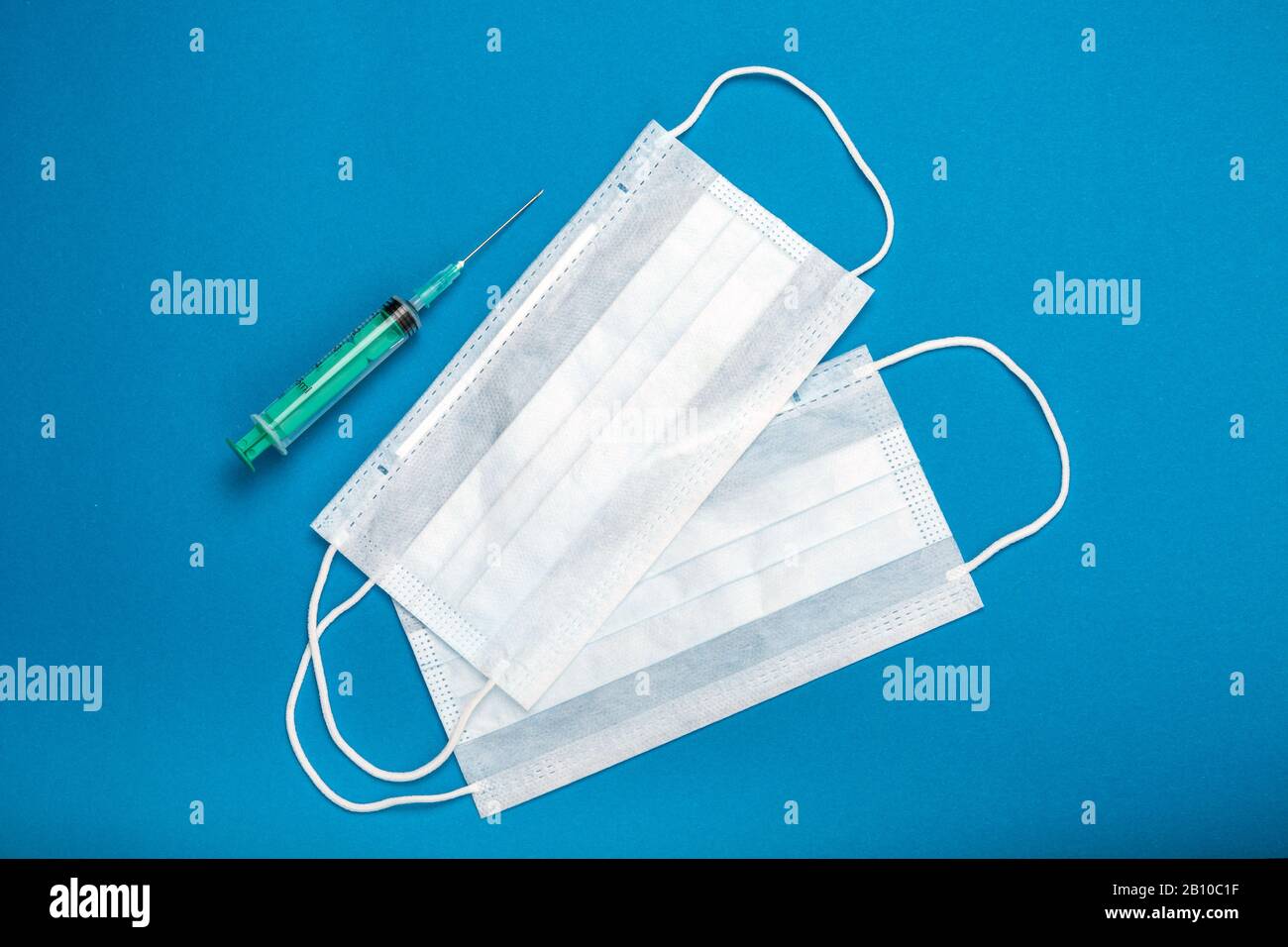 Green syringe and two surgical masks with rubber ear straps. Typical 3ply surgical mask to