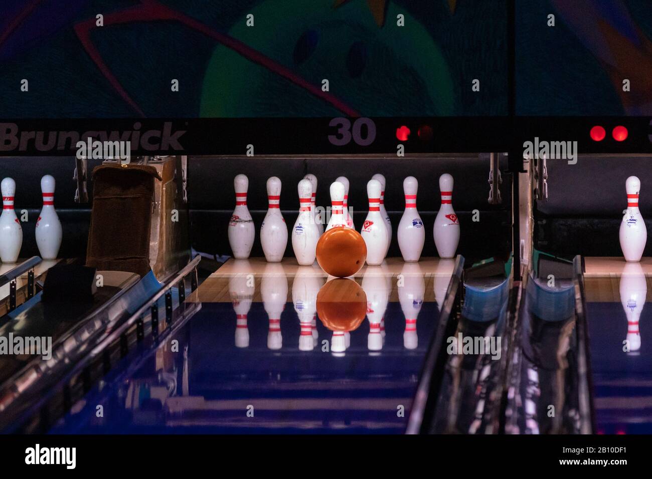 Hillsboro, Oregon  USA - March 16, 2019: Orange bowling ball is to hit the center of pins at the end of a bowling alley reflecting on a polished lane Stock Photo