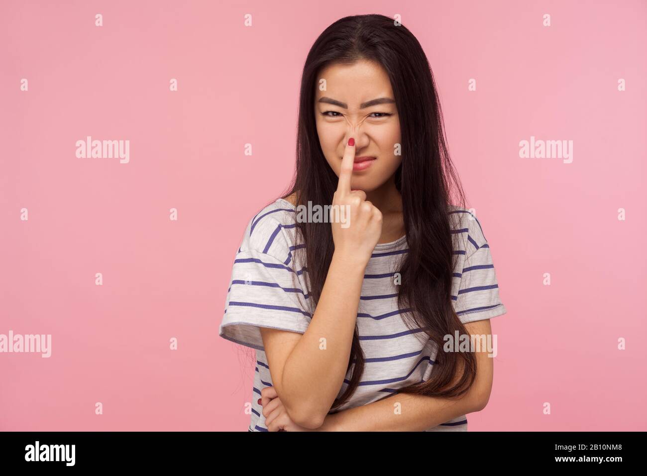 This is lie! Portrait of girl with long hair in striped t-shirt touching nose, gesturing you are liar, being distrustful of talk, suspecting falsehood Stock Photo