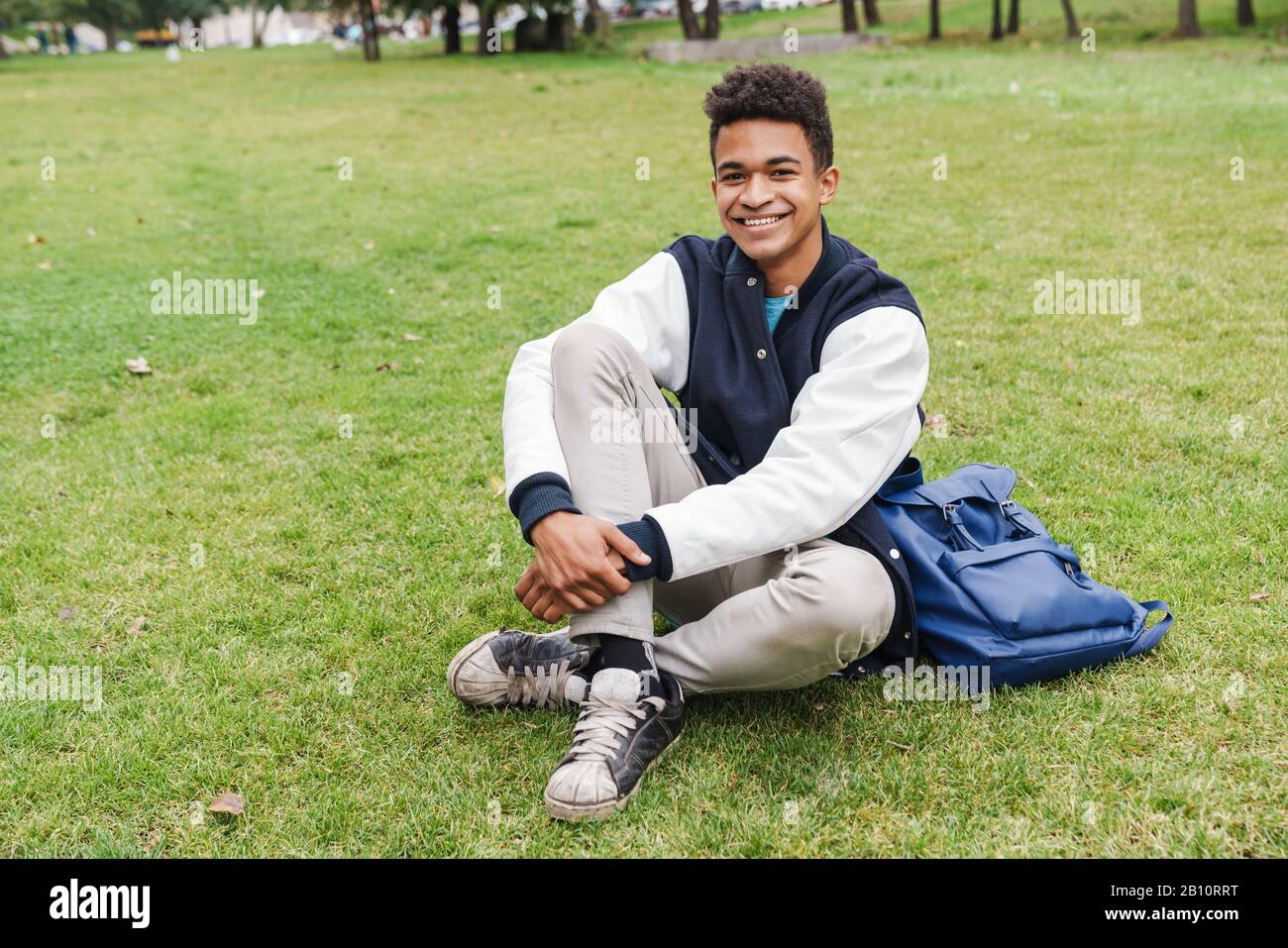 Happy teenager student boy sitting on a lawn at the park Stock Photo ...
