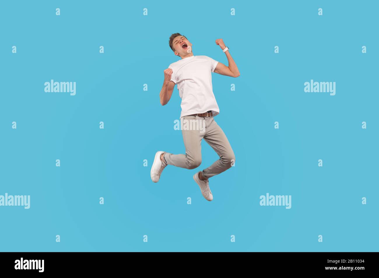 Full length, excited successful man in white t-shirt and casual pants jumping with happiness and shouting yes, I did it, feeling inspired and energeti Stock Photo