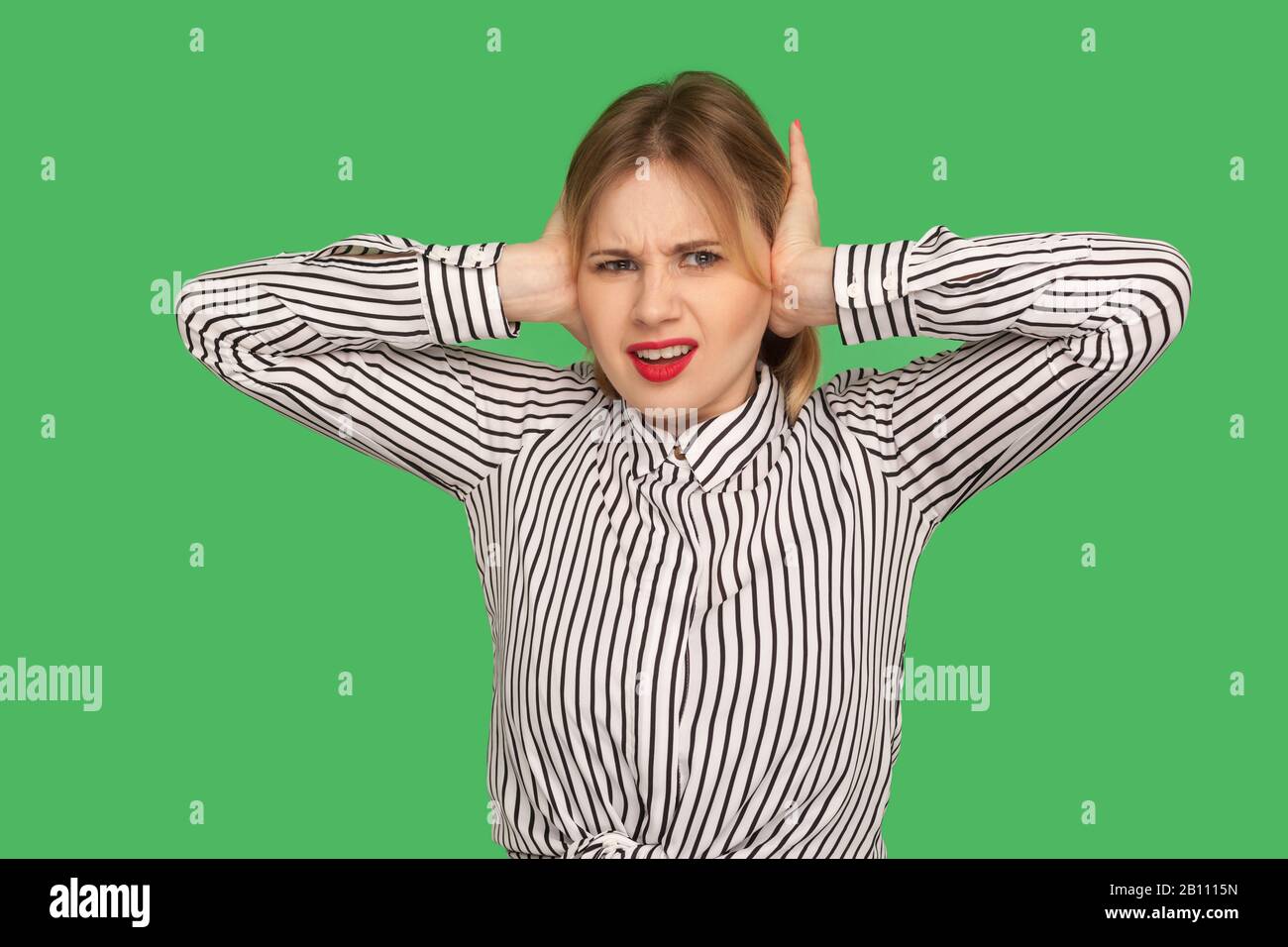 Don't want to listen anymore. Angry irritated blond girl in blouse covering ears with hands to stop hear annoying talk, avoiding high-decibel sound. i Stock Photo