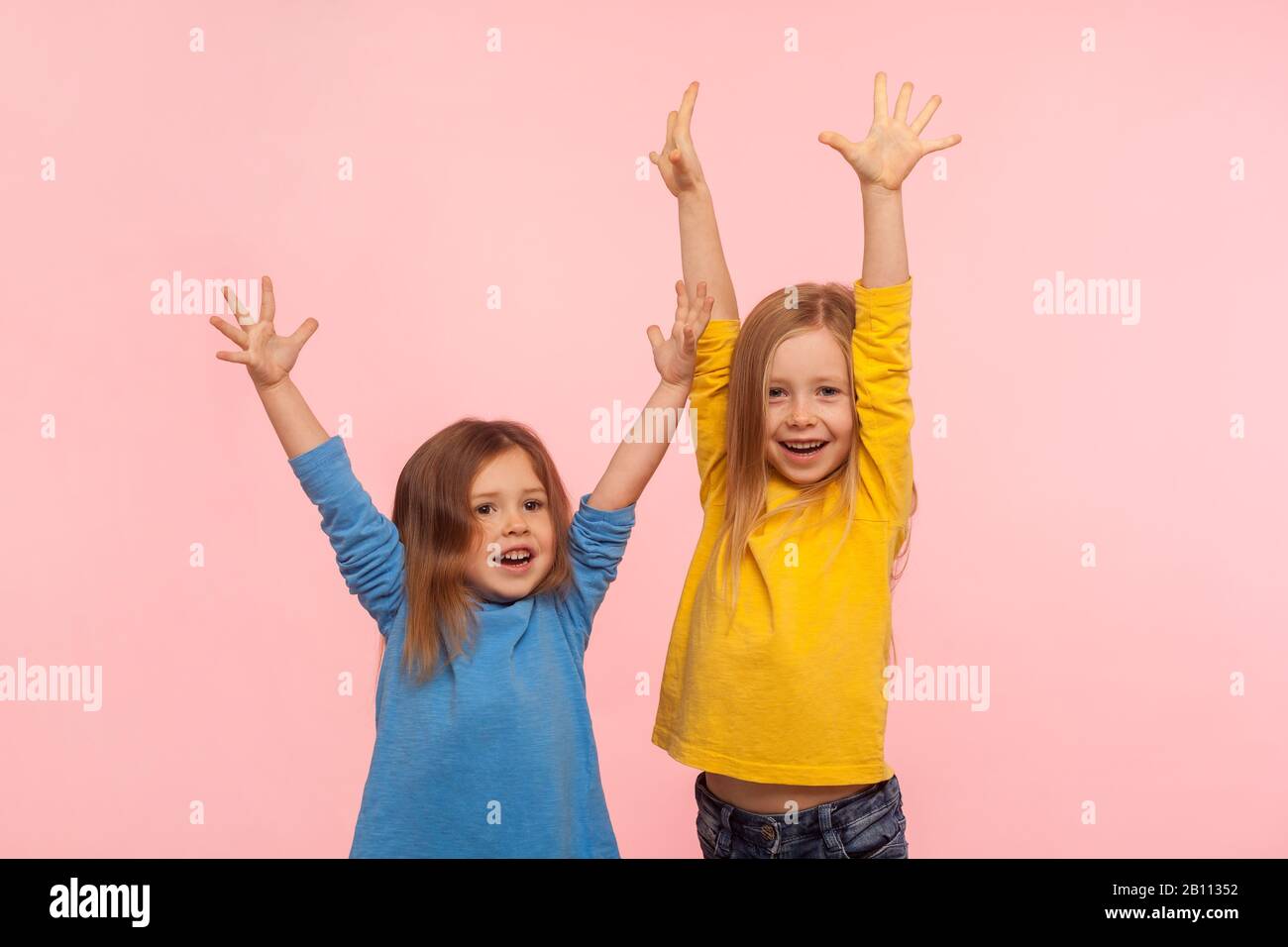 Emotions of happy winners children. Two enthusiastic lively energetic little girls standing with raised hands and screaming for joy, celebrating victo Stock Photo