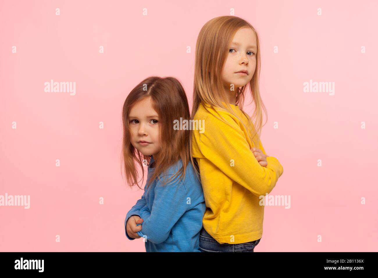 Friendship, togetherness and support. Two wonderful preschool girls standing back to back, looking at camera with confident attentive serious expressi Stock Photo