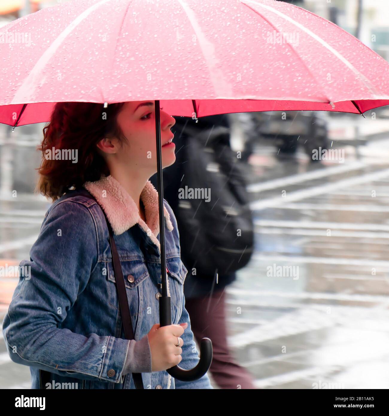 Belgrade, Serbia - September 24, 2019: One young woman in denim jacket walking under red umbrella on a rainy day Stock Photo