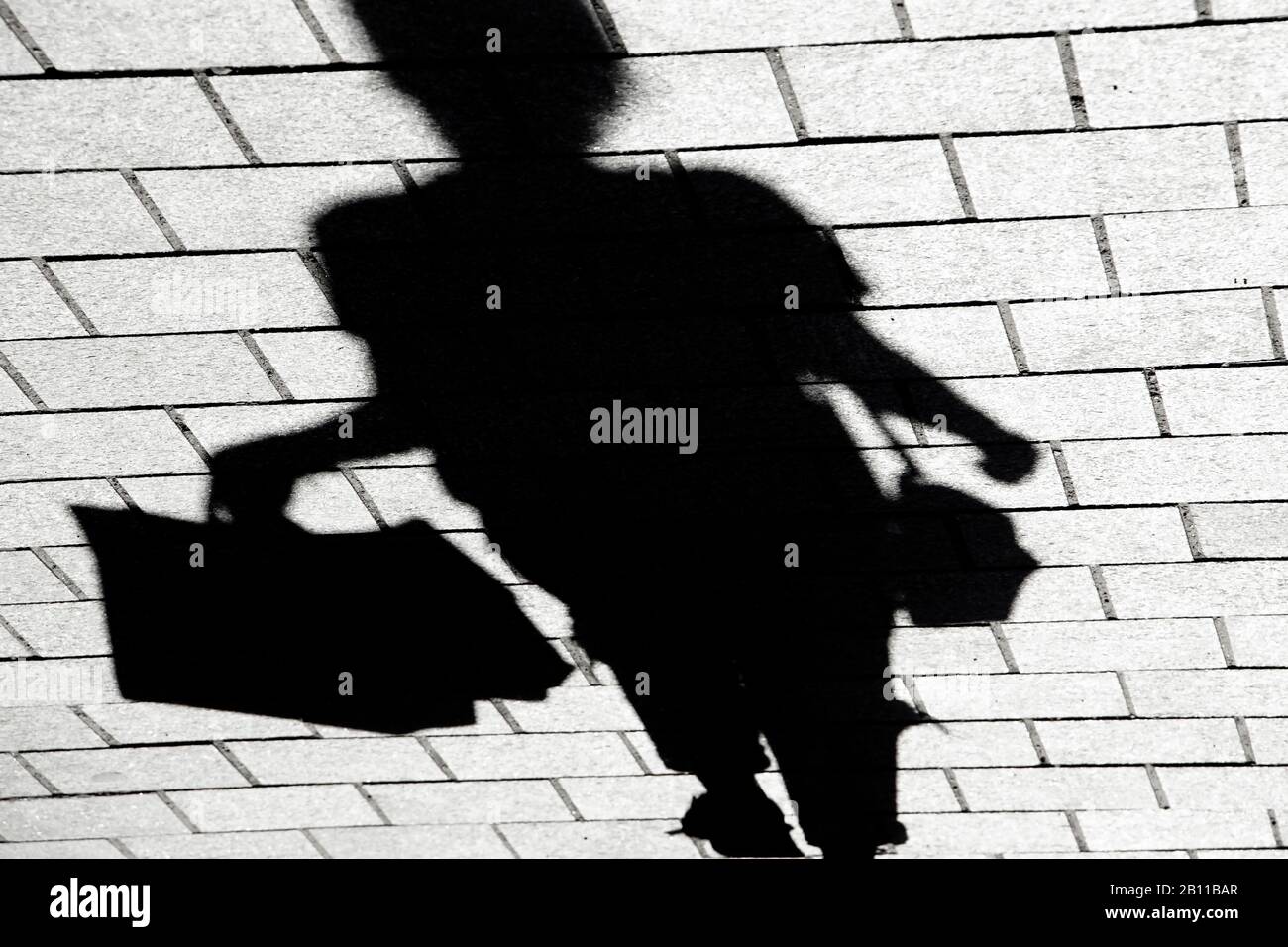 Blurry shadow silhouette of a young woman walking alone on city street sidewalk with shopping bags in high contrast black and white, upside down Stock Photo