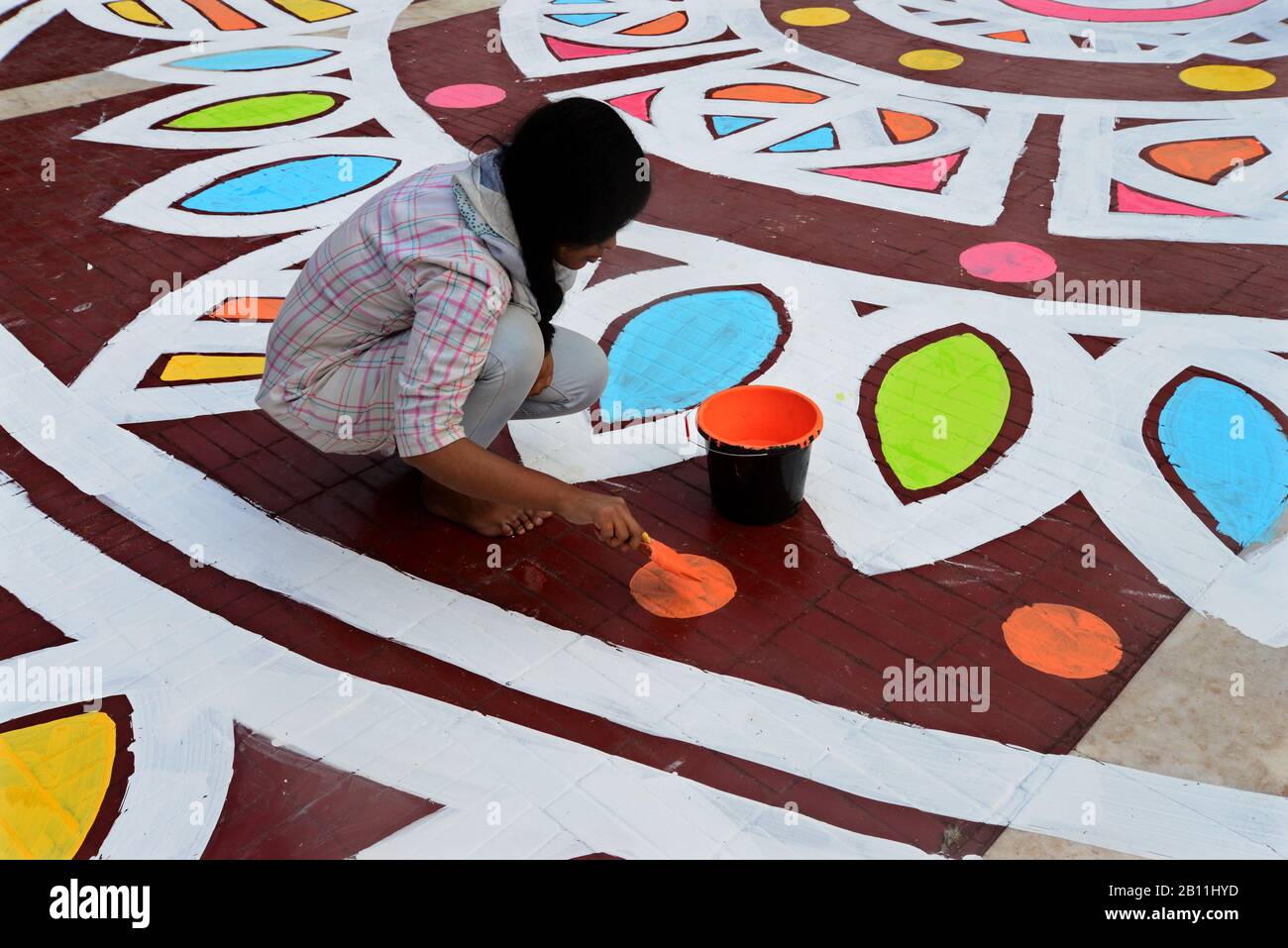 Bangladeshi fine arts students paint a design on the ground in front of