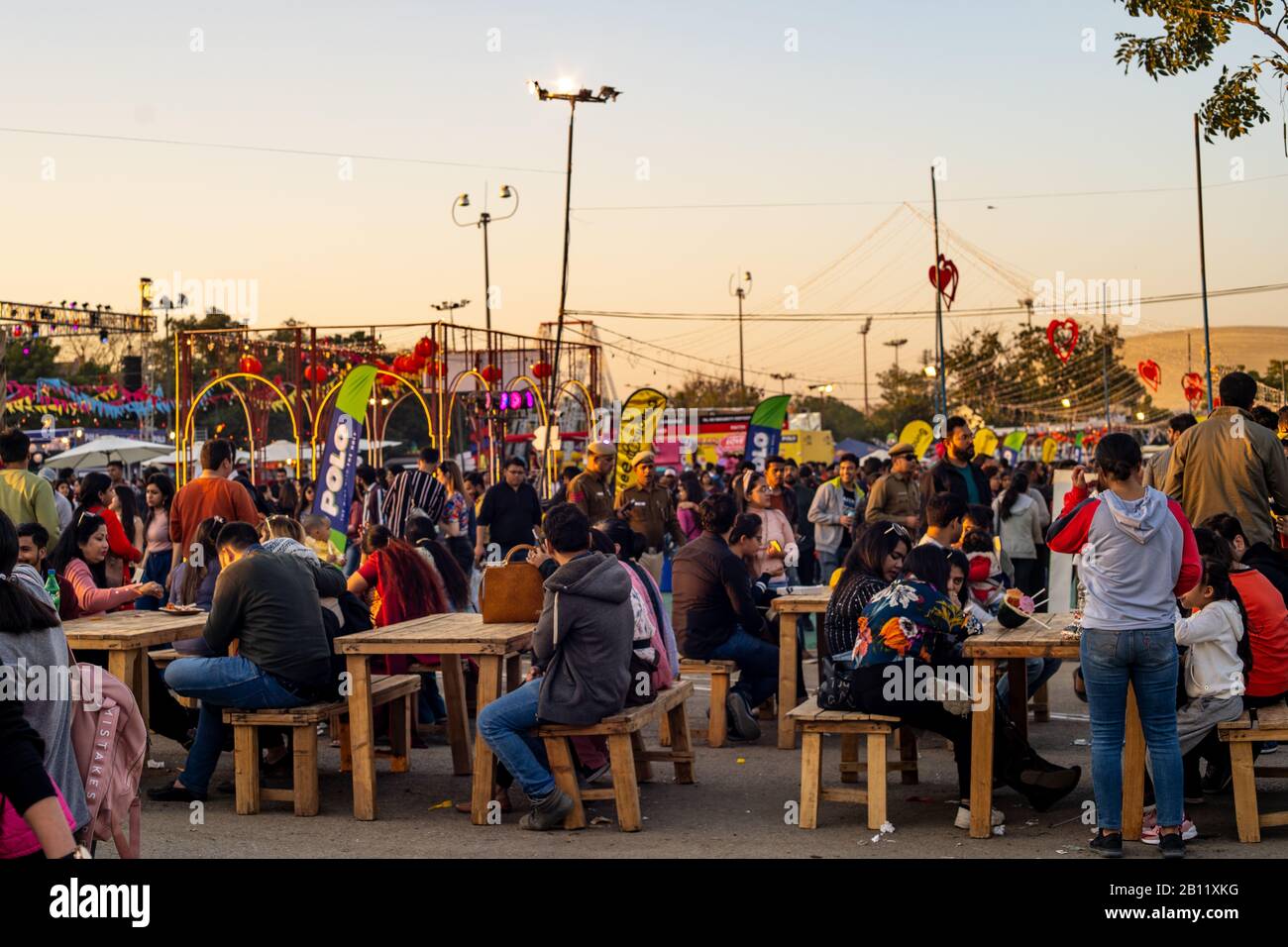 Panning shot of crowd of people roaming around sitting on old tables and benches while they eat Stock Photo