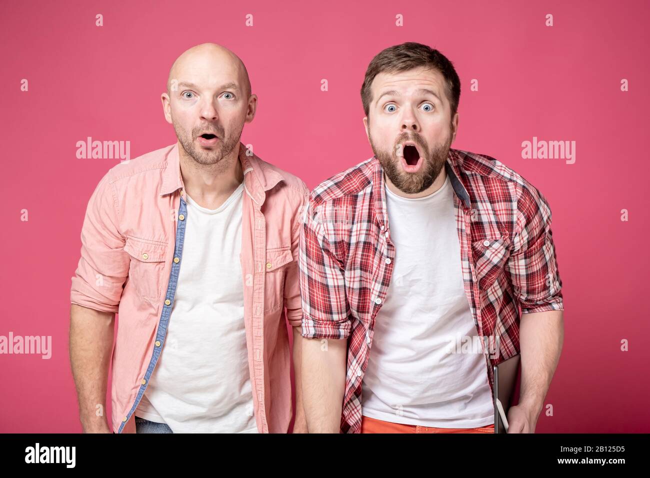 Two men are shocked, they open their mouths in amazement and look at the camera with big eyes, with interesting excited faces. Stock Photo