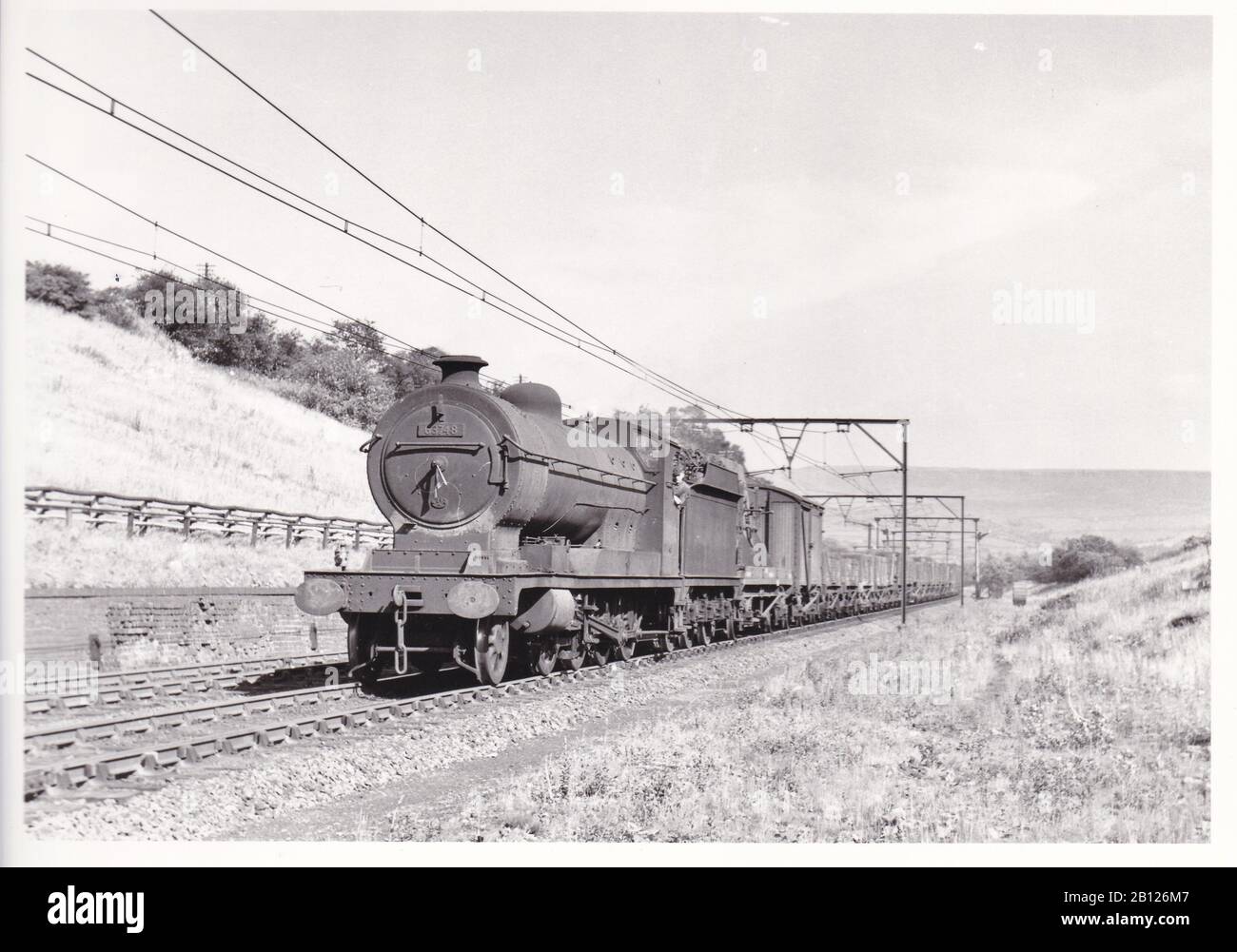 Vintage black and white photo of steam locomotive train - E.R. Class 04/7 2-8-0 63748 on a down freight near Godley East Junction May 1954. Stock Photo