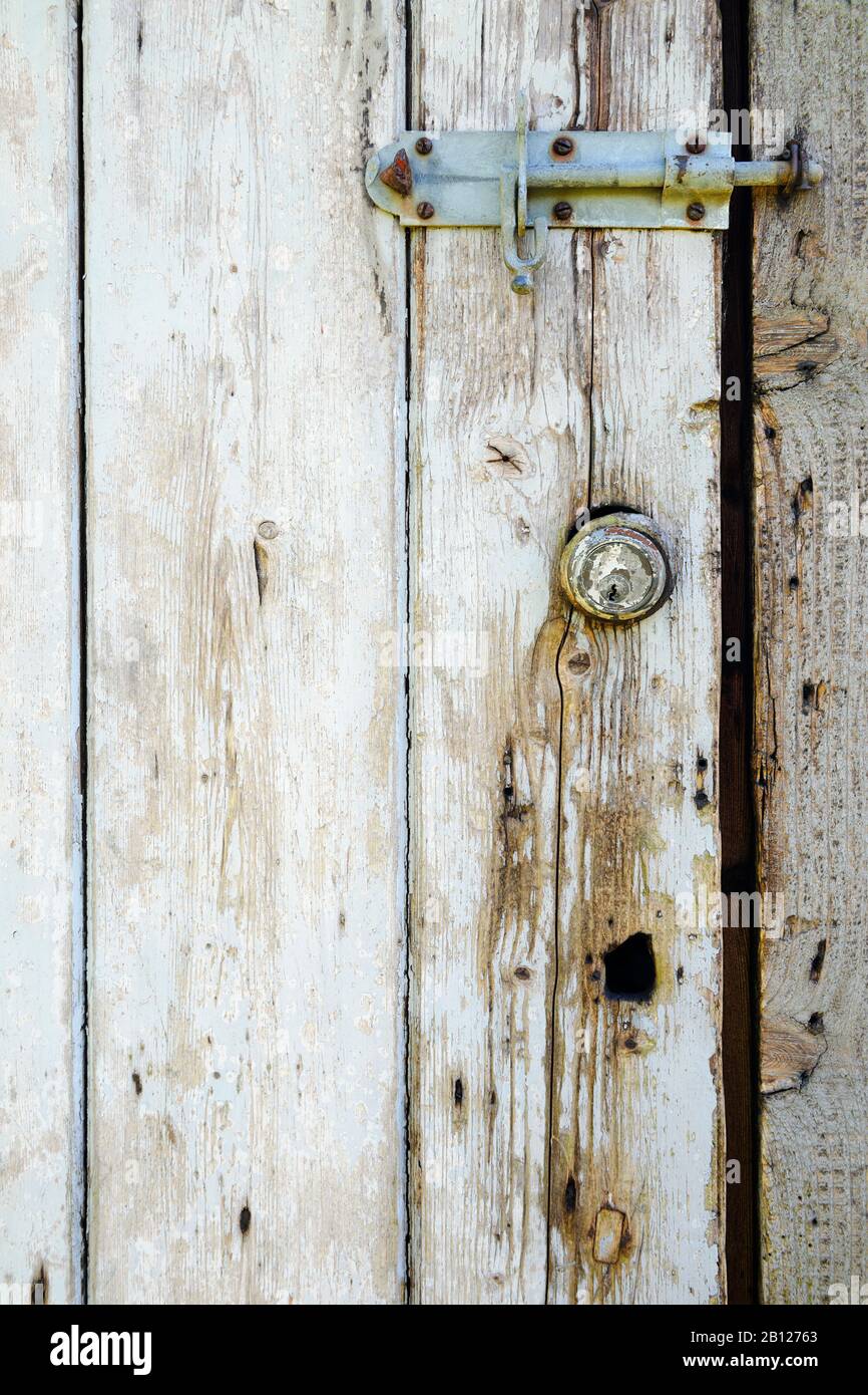 Old Yale cylinder lock in weathered, painted wooden door, reused as chicken shed door. Stock Photo