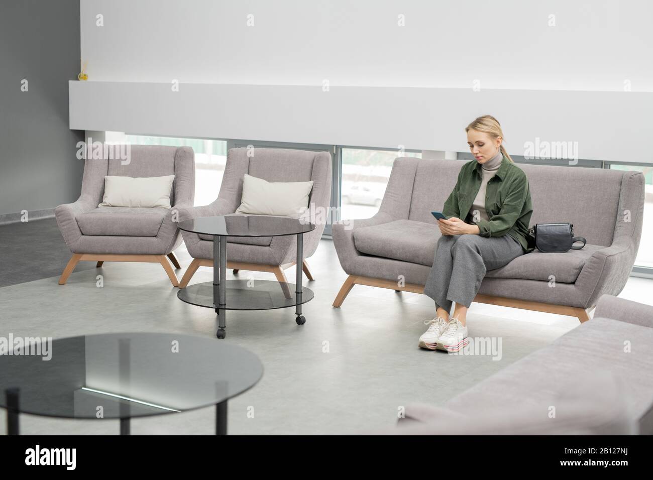 Young blond female in casualwear sitting on couch inside medical center Stock Photo