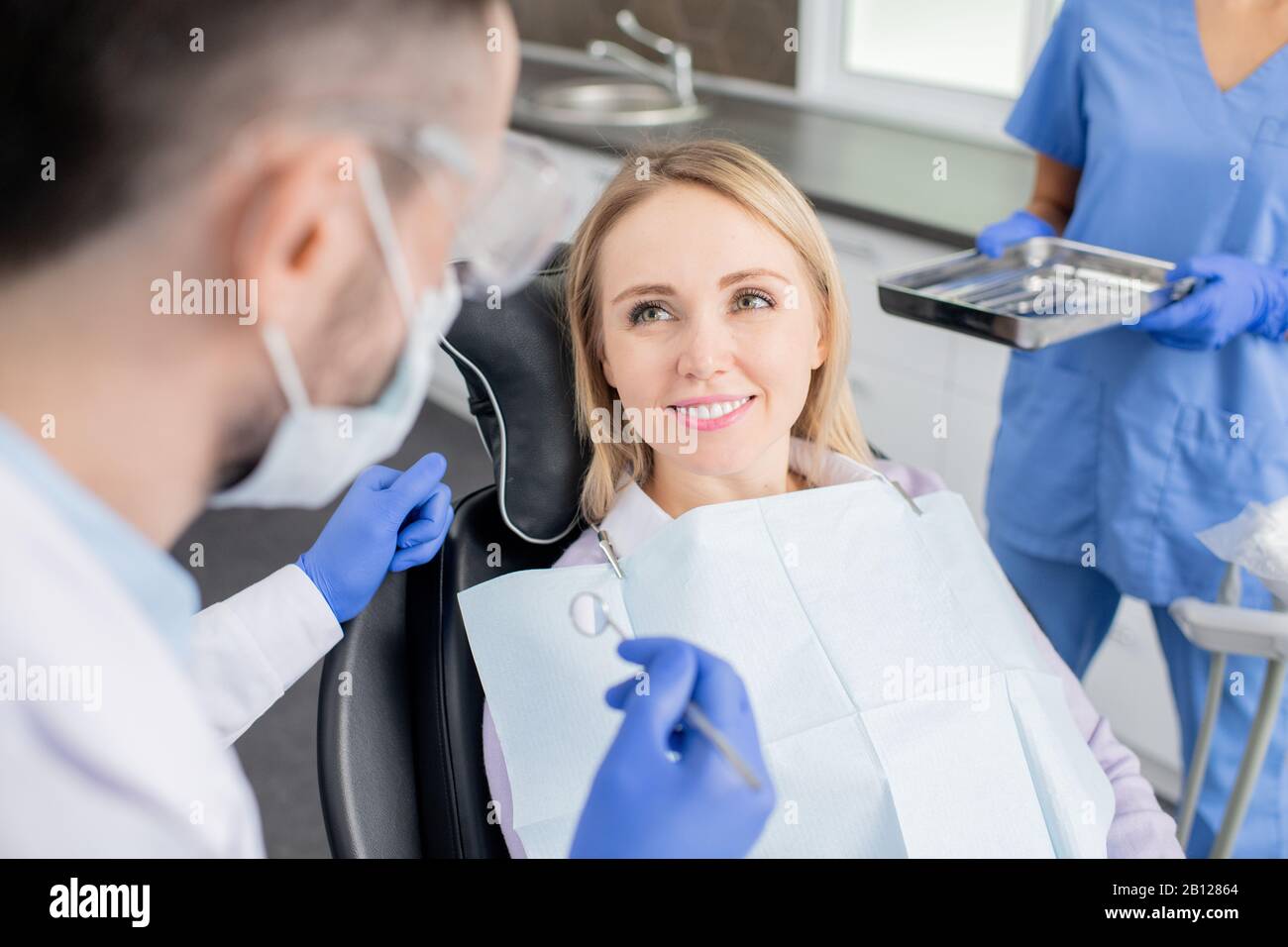 Happy young woman looking at her dentist with toothy smile before examination Stock Photo