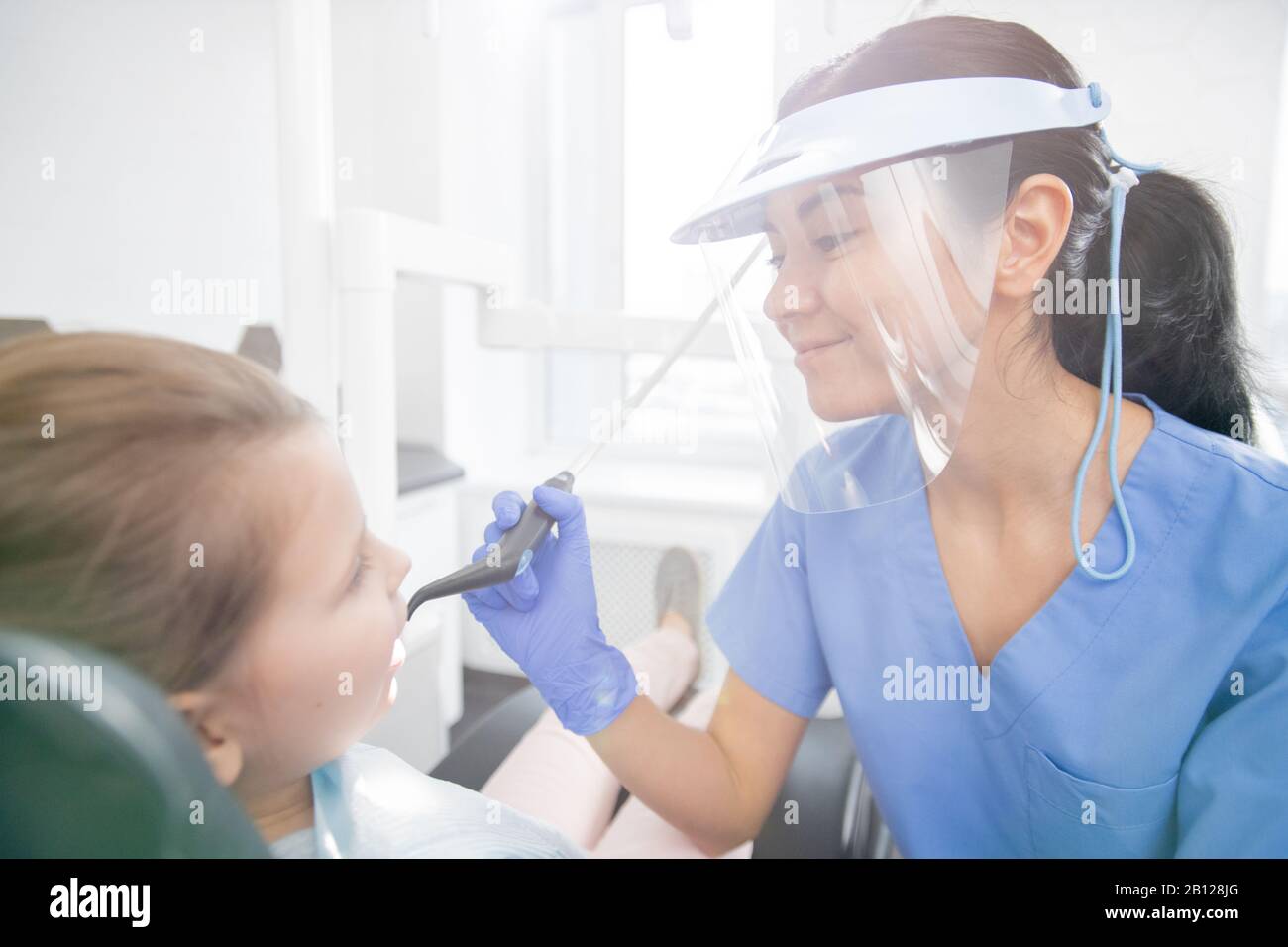 Young female dentist going to repair teeth of little girl after oral examination Stock Photo