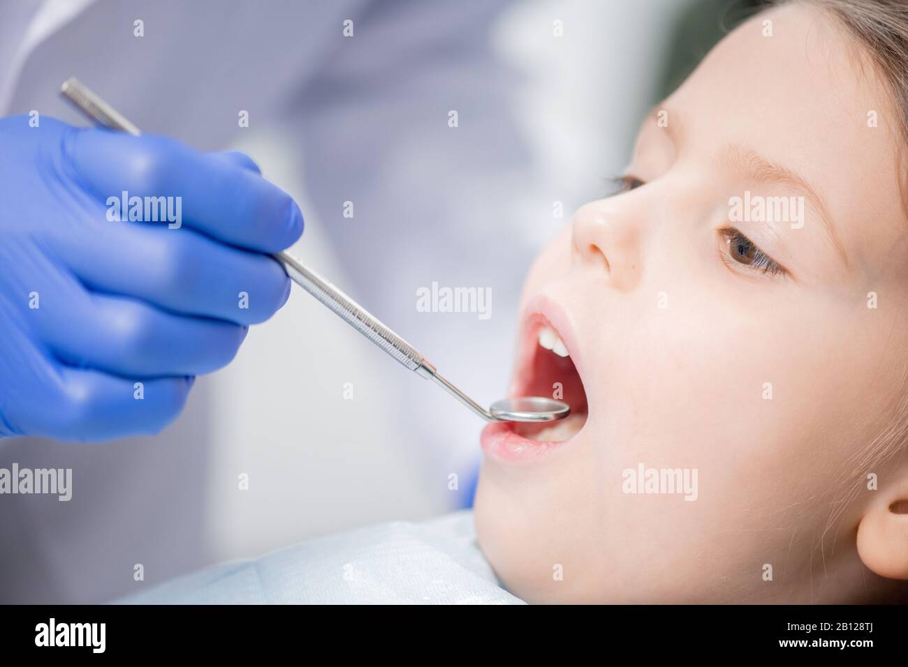 Gloved hand of dentist examining teeth of cute little patient with dental mirror Stock Photo