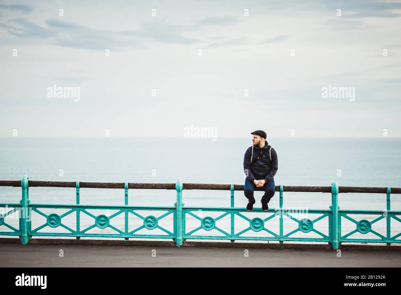 Tourist sits on a railing on the seafront, Brighton Beach, Brighton, England | Stock Photo Tourist sits on a railing on the seafront, Brighton Beach, Brighton, England Stock Photo