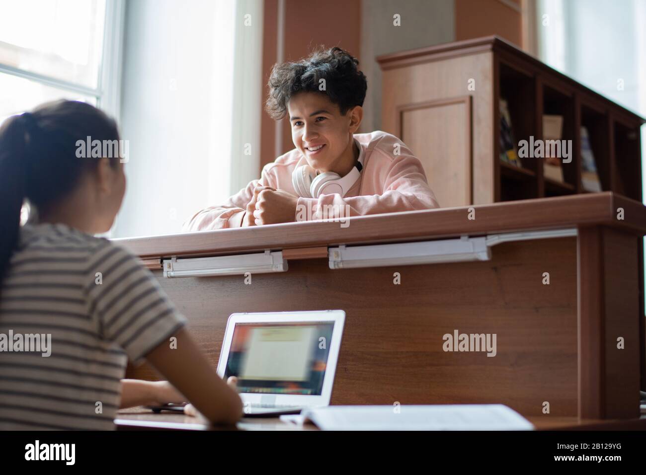 Cheerful teenage boy looking at his groupmate with laptop while asking for help Stock Photo