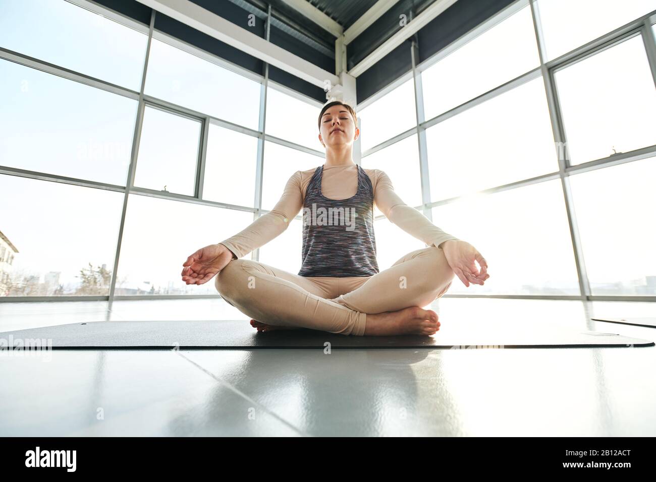 Young relaxed woman in activewear sitting in pose of lotus with crossed legs Stock Photo