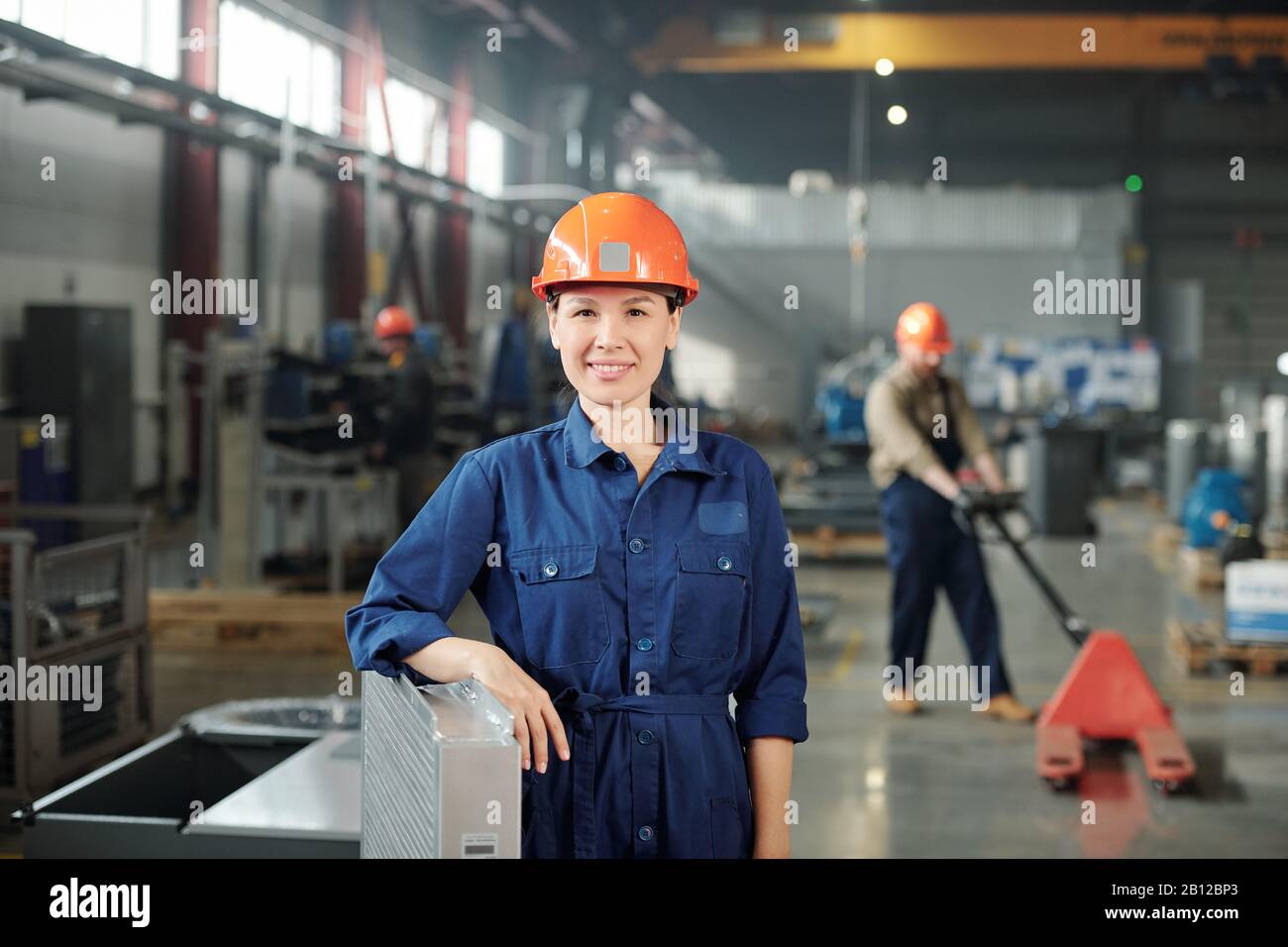 Happy young smiling female engineer in hardhat and blue coveralls Stock Photo