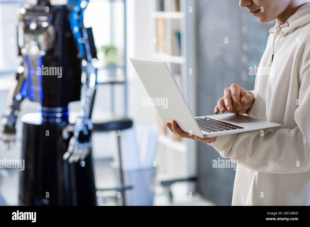 Young man in hoodie using laptop during presentation or testing automation robot Stock Photo