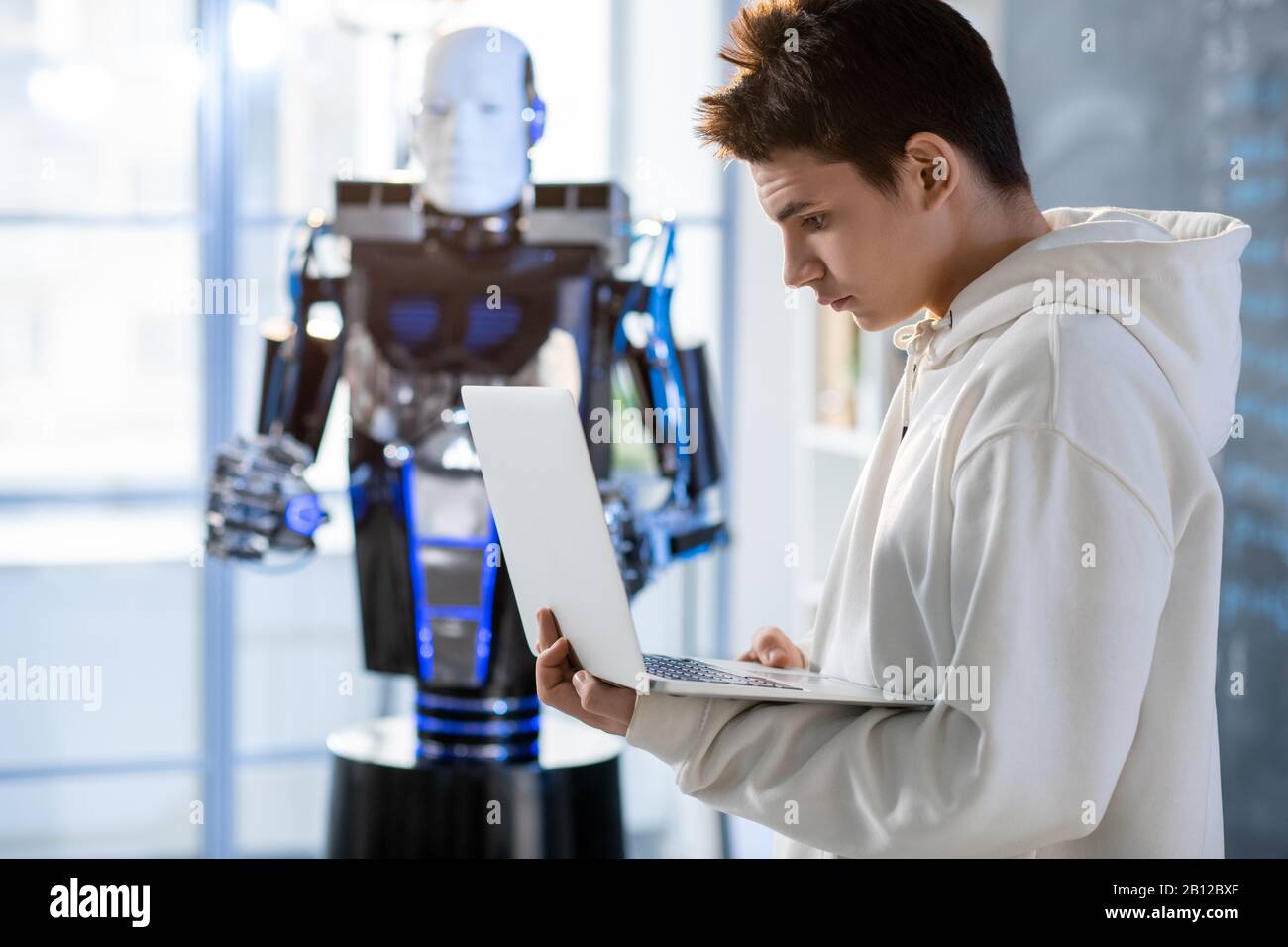Young student looking at laptop display while working with automation robot Stock Photo