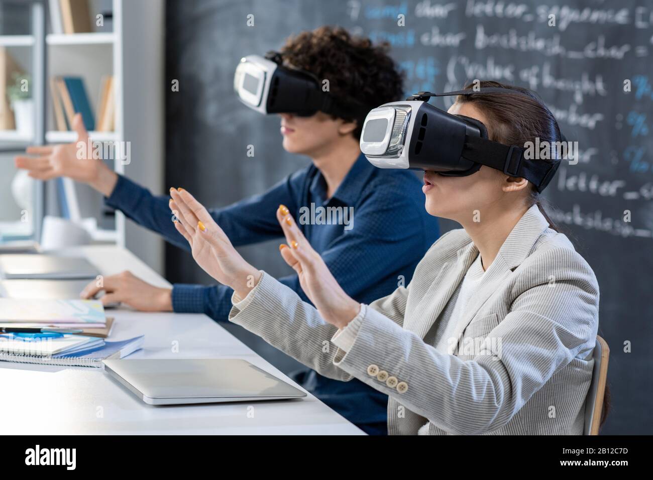 One of two students in vr headsets touching virtual display during presentation Stock Photo