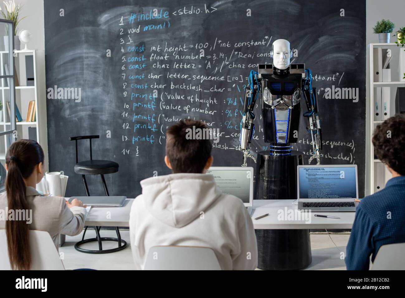 Rear view of row of students sitting by desk in front of automation robot Stock Photo