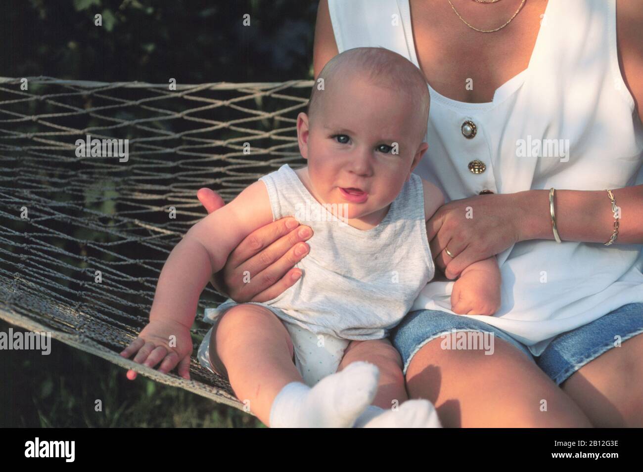 8 months old baby, wearing diapers, sitting with his mother in hammock