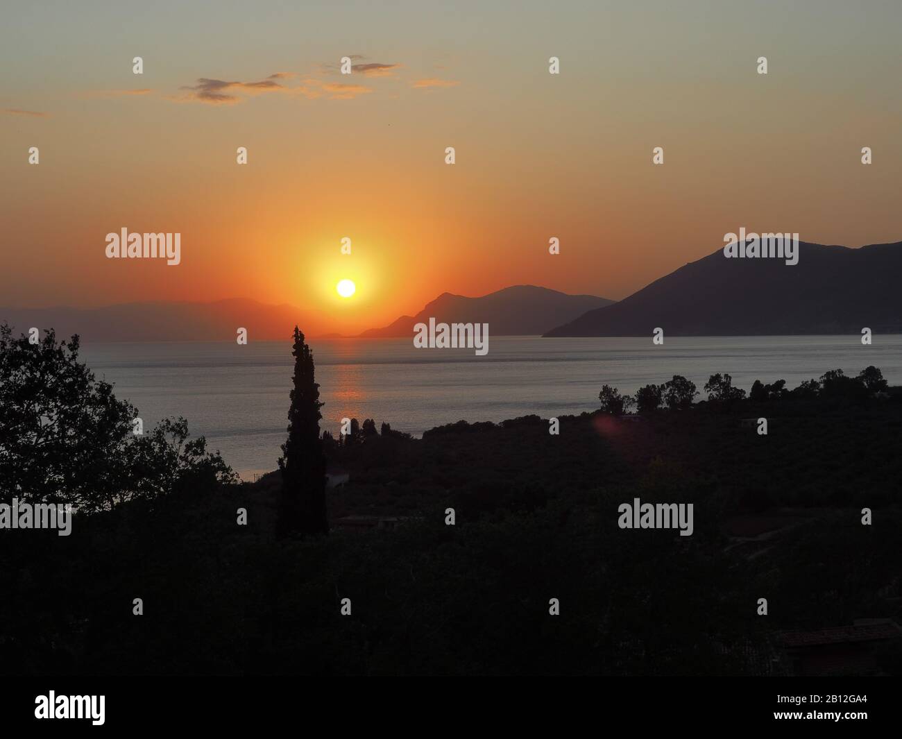 Sun setting between the mountains as seen across the sea from Rovies, Evia, Greece Stock Photo