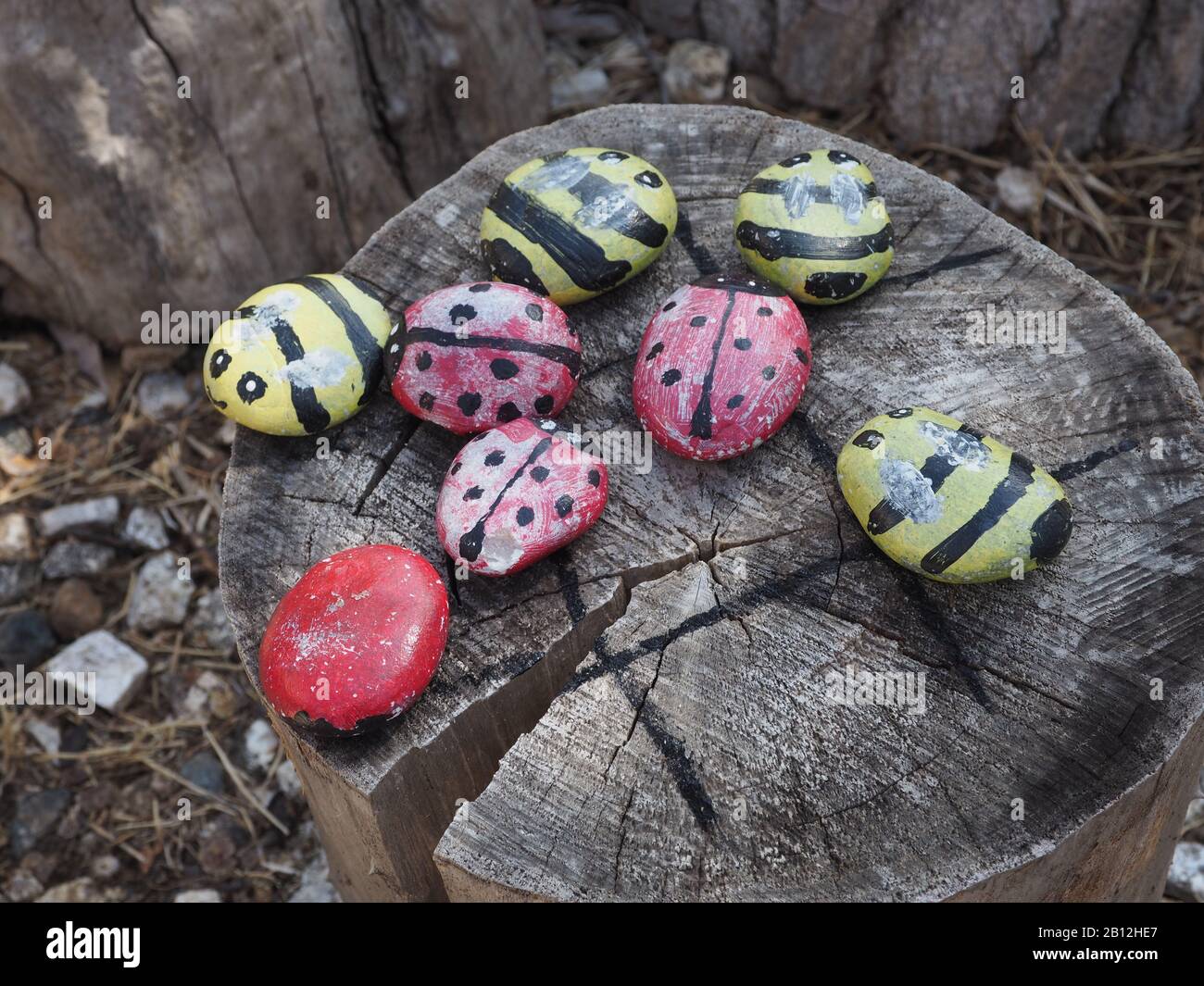 Stones painted to look like insects on a table made from a log Stock Photo