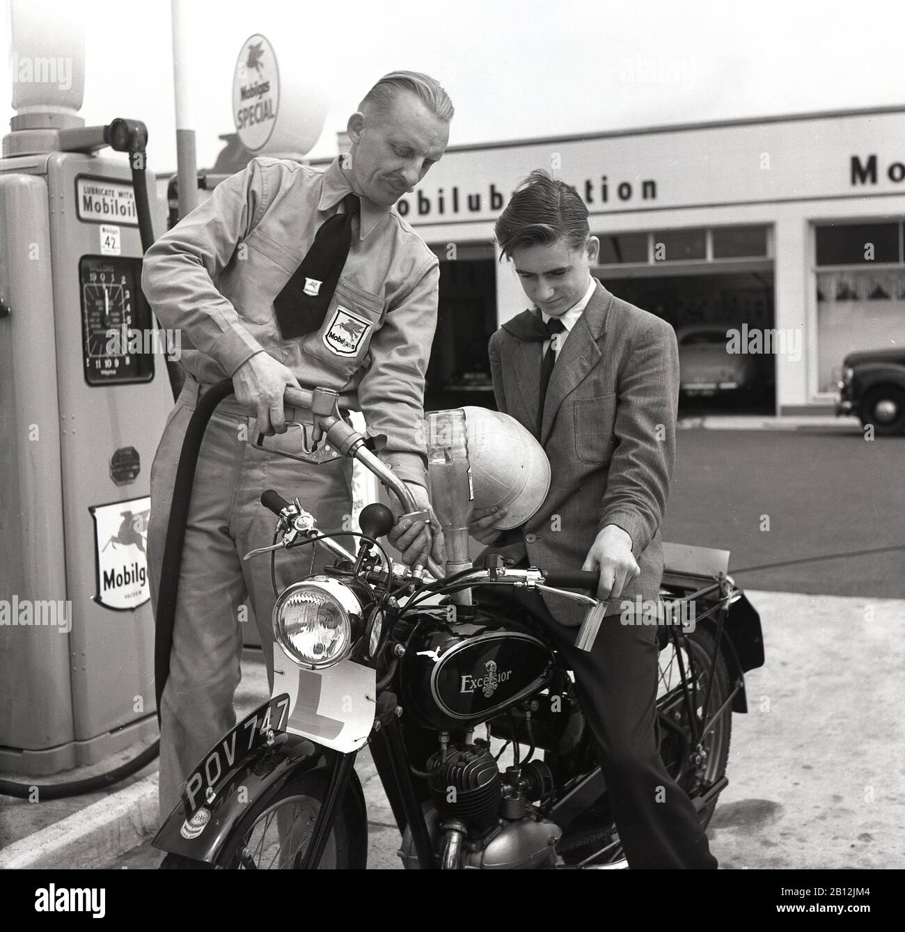 1950s, historical, a young male motorcyclist parked by the fuel pumps at a garage getting fuel and oil for his Excelsior motorcycle by a uniformed  forecourt attendant, London, England, UK. As motoring increased in post-war Britain, larger garages or 'service stations' were opened offering a range of motor-related services including manned forecourt attendants. Based in Coventry, England, Excelsior were Britain's first motorcycle manufacturer, producing their own 'motor-bicycle' in 1896. Stock Photo