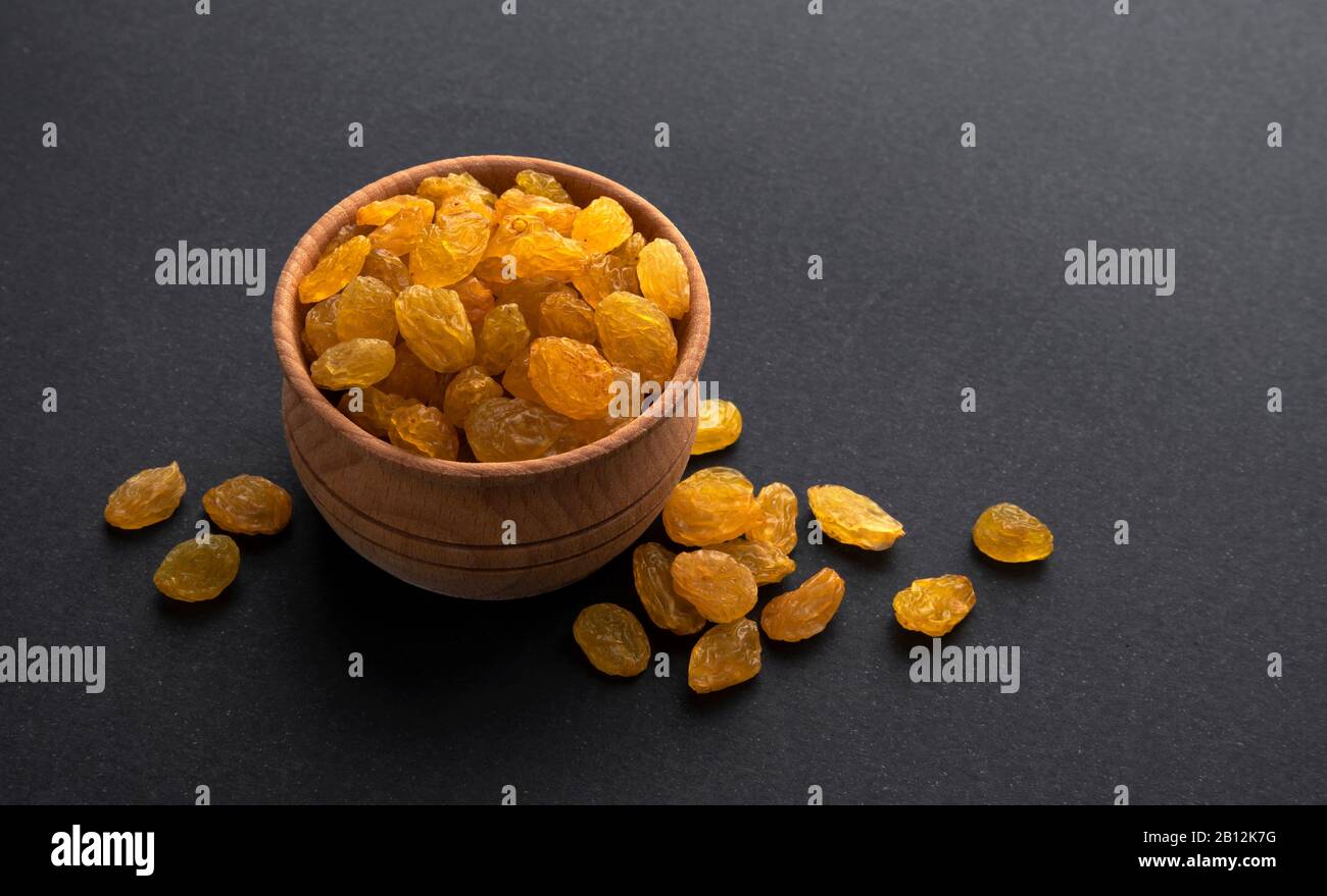 Yellow raisins in wooden bowl on black background Stock Photo