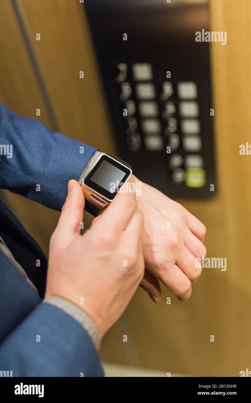 Man with smartwatch on his hand with elevator control panel in the background. Stock Photo