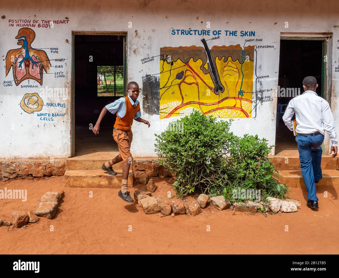 A pupil leaving and a teacher entering classrooms at a rural junior school near Voi in Southern Kenya Stock Photo