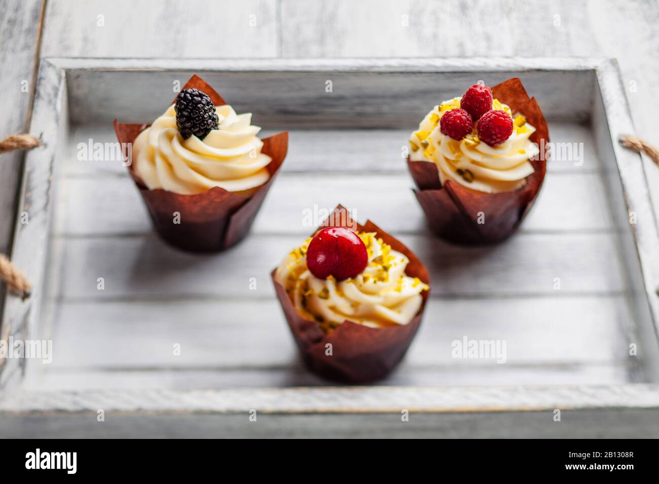 muffins with Belgian chocolate and white chocolate cream and mascarpone with berries on a wooden tray Stock Photo