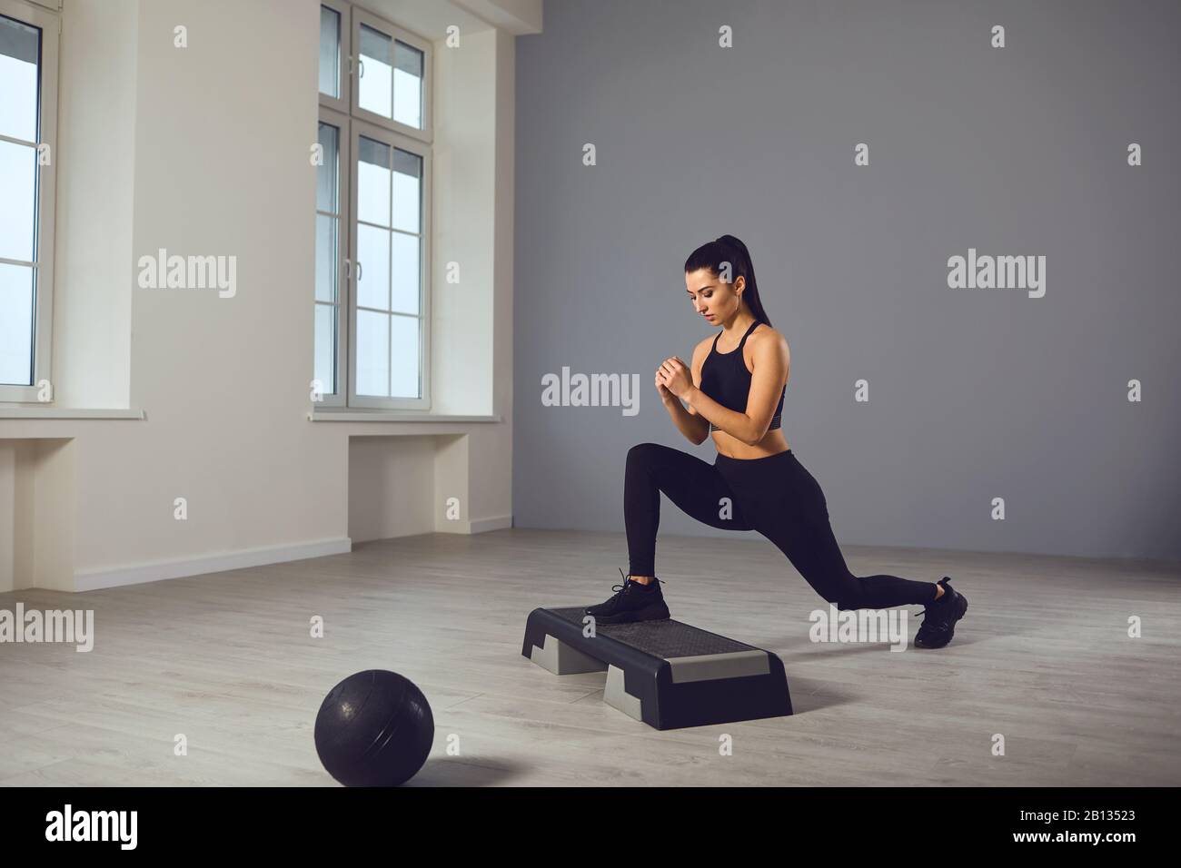 Squat exercises. Girl in black sportswear with dumbbells in her hands doing squats in a room. Stock Photo