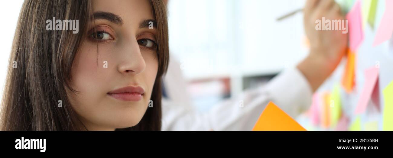 Pretty female office worker holding sticky paper looking in camera Stock Photo