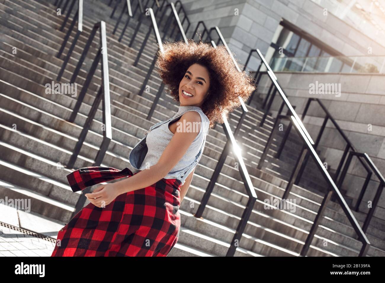 Young woman in the city street standing on stairs smiling cheerful Stock Photo