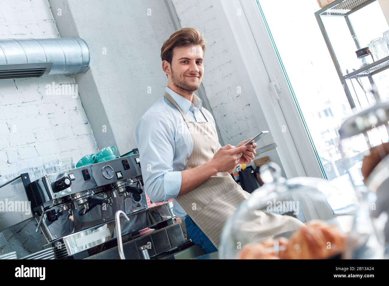 Young adult barista working in restaurant, using modern tablet Stock Photo