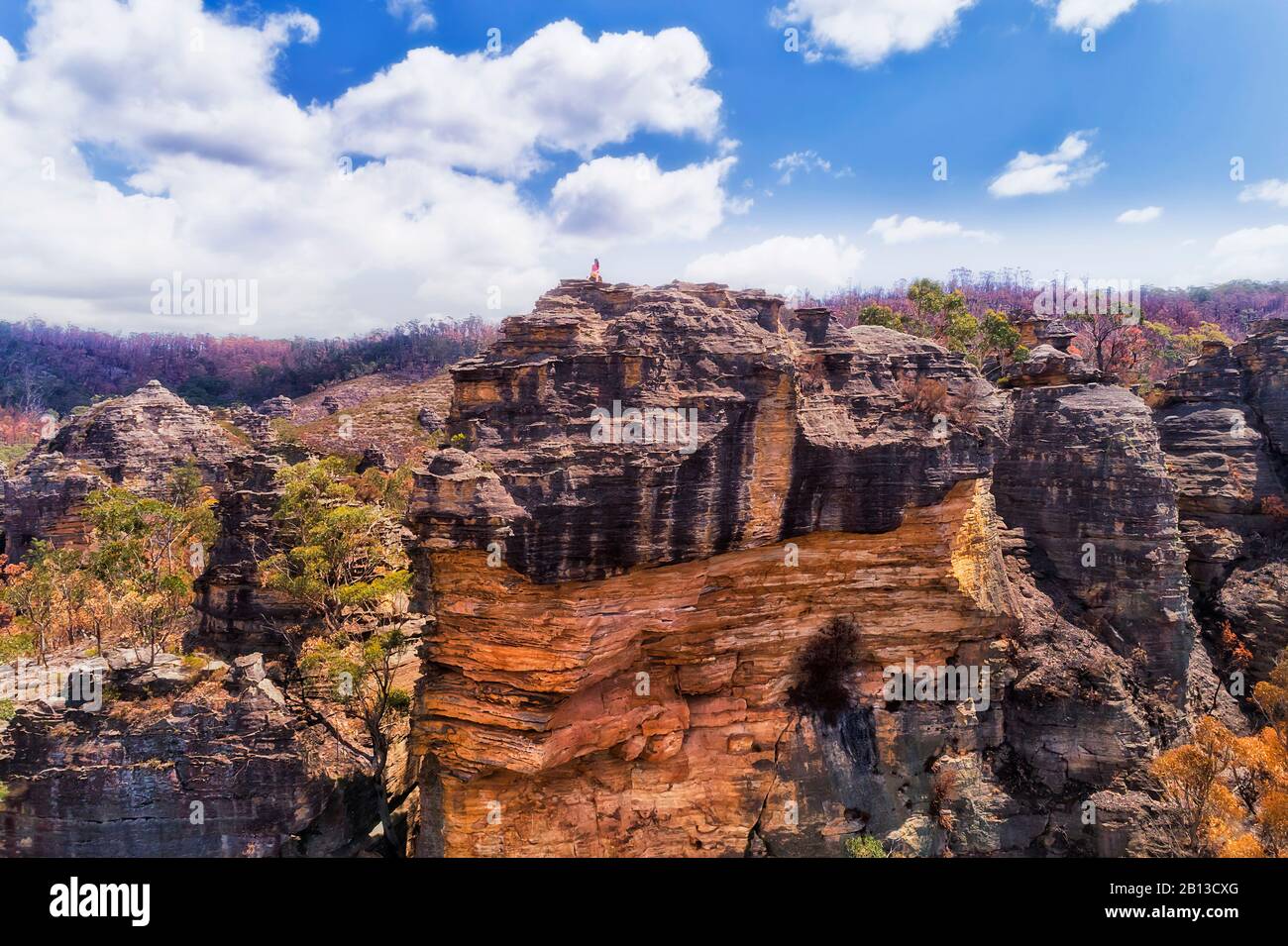 Sharp steep cliff of sandstone rocks in Blue Mountains of Australia. Lonely girl sits on the top. Stock Photo