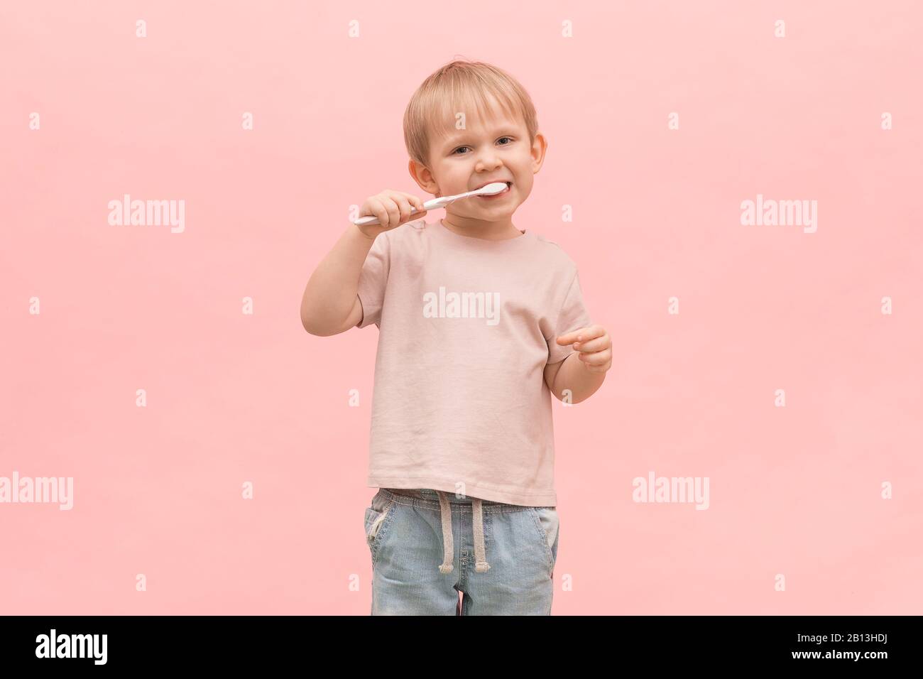 Child boy blond brushes his teeth with a toothbrush on a pink background. Concept for articles on healthy gums, oral hygiene and treatment in dentistr Stock Photo