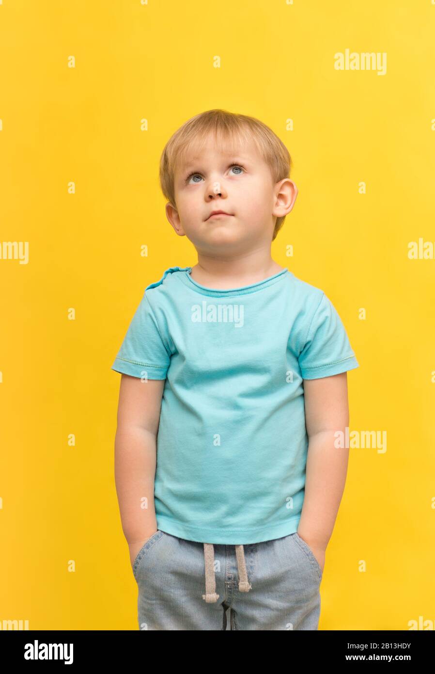 A charismatic handsome blond boy stands and looks upstairs on a yellow spring bright background with place for text. Concept for banner, handout of pr Stock Photo