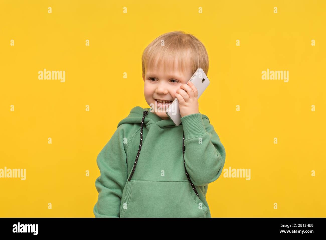 Child boy blond talking on the phone smartphone on a yellow spring background. Concept for articles about modern childhood, children's communication, Stock Photo