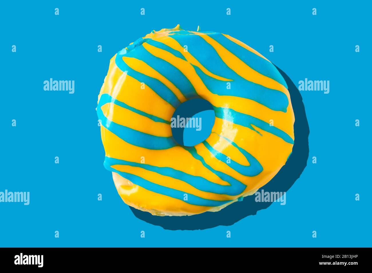 Colorful bright yellow and blue glazed  appetizing doughnut on bright blue  background. Top view of yummy looking donut. Stock Photo
