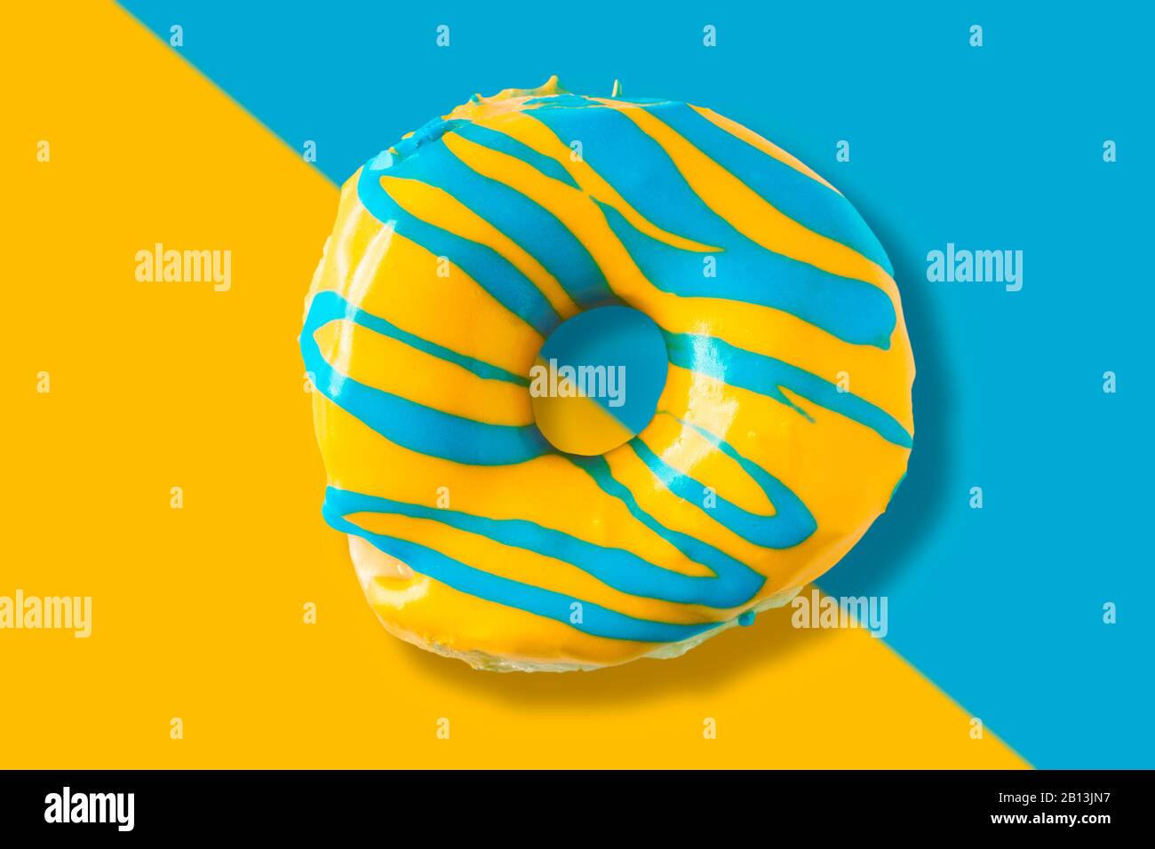 Colorful bright yellow and blue glazed  appetizing doughnut on split color background. Top view of yummy looking donut. Stock Photo