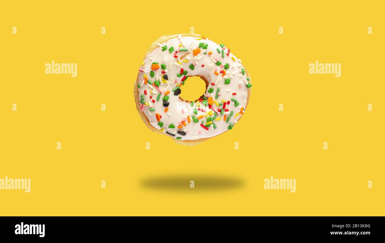 Delicious levitating donuts with white frosting and colorful sprinkles on bright yellow background. Large close up doughnut Stock Photo
