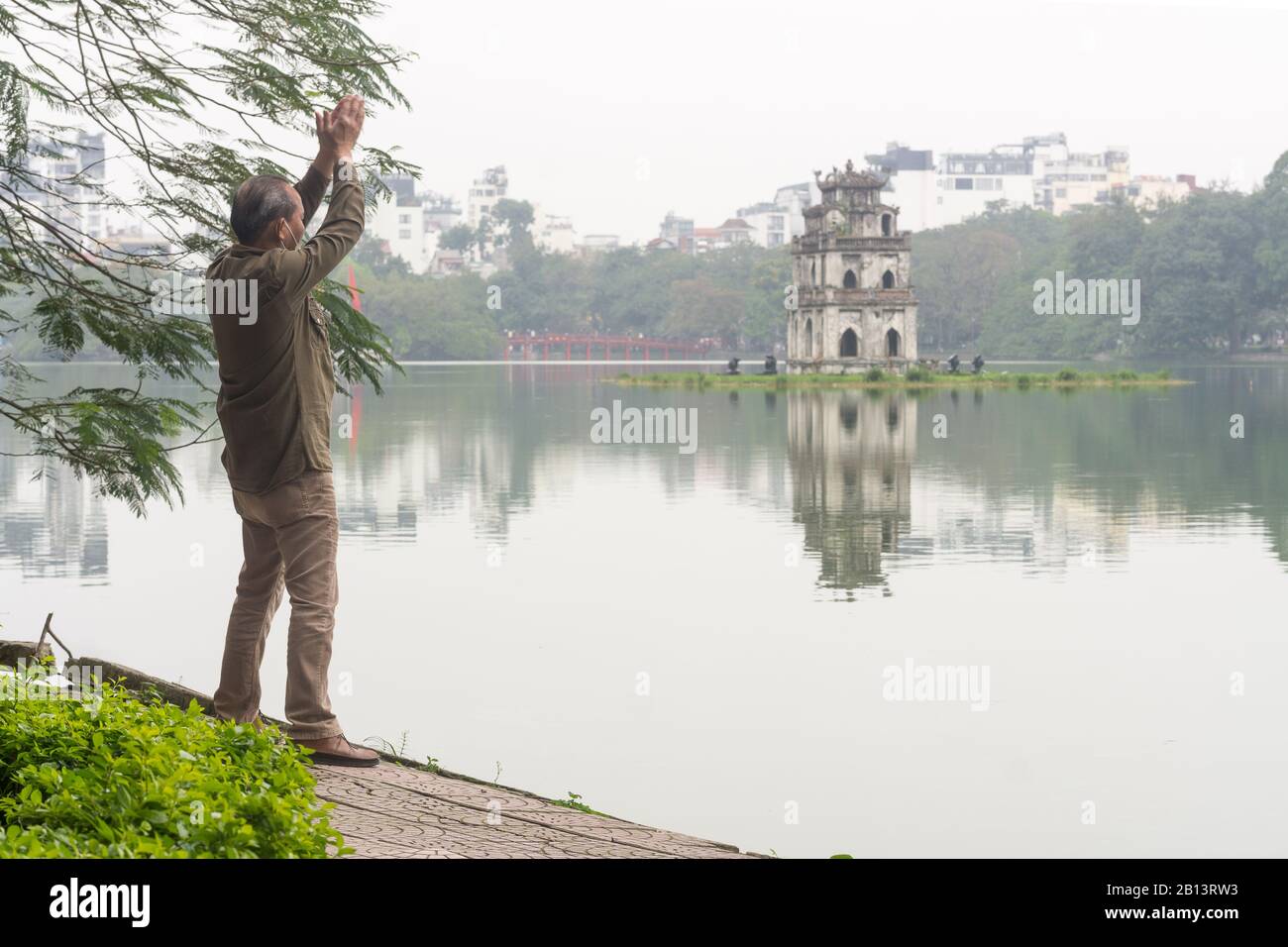 Hoan Kiem Lake Hanoi - Elderly Vietnamese man exercising near Hoan Kiem Lake in Hanoi with Turtle Tower in the background, Vietnam, Stock Photo