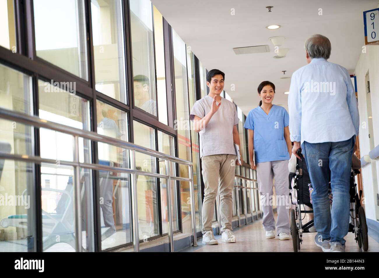 happy young asian physical therapists greeting residents in hallway of nursing home Stock Photo