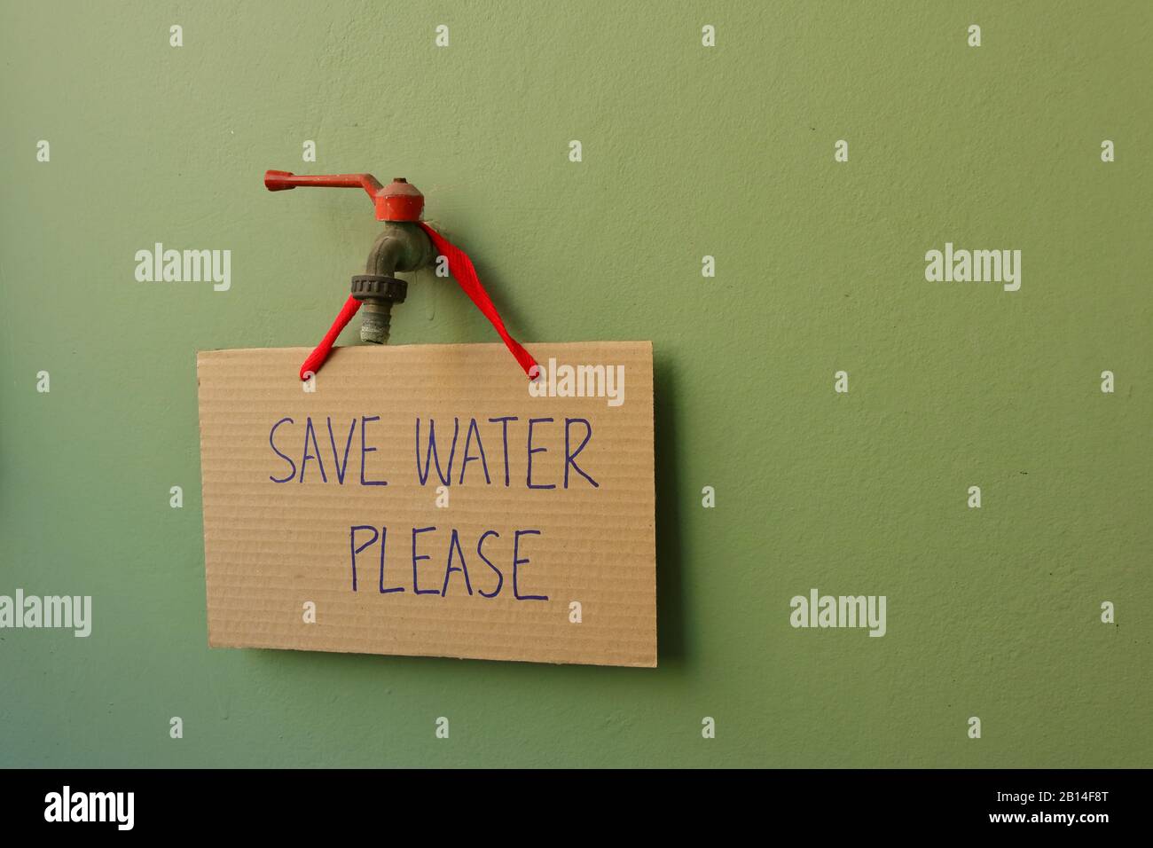 Closeup cardboard sign with handwriting SAVE WATER PLEASE hanging on old faucet installed on green wall, water conservation concept Stock Photo